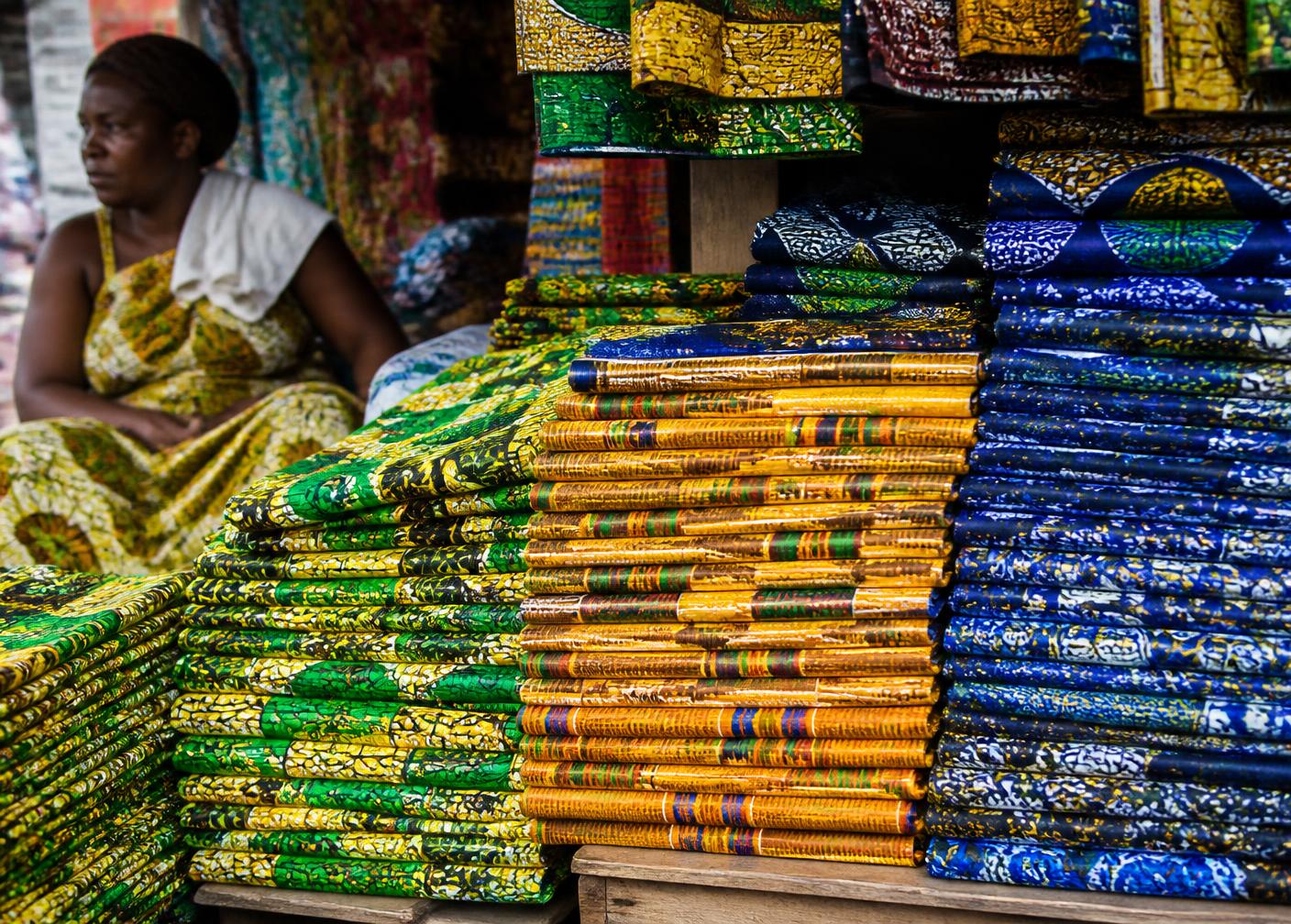 Wax print and kente fabric stacked at an Accra market